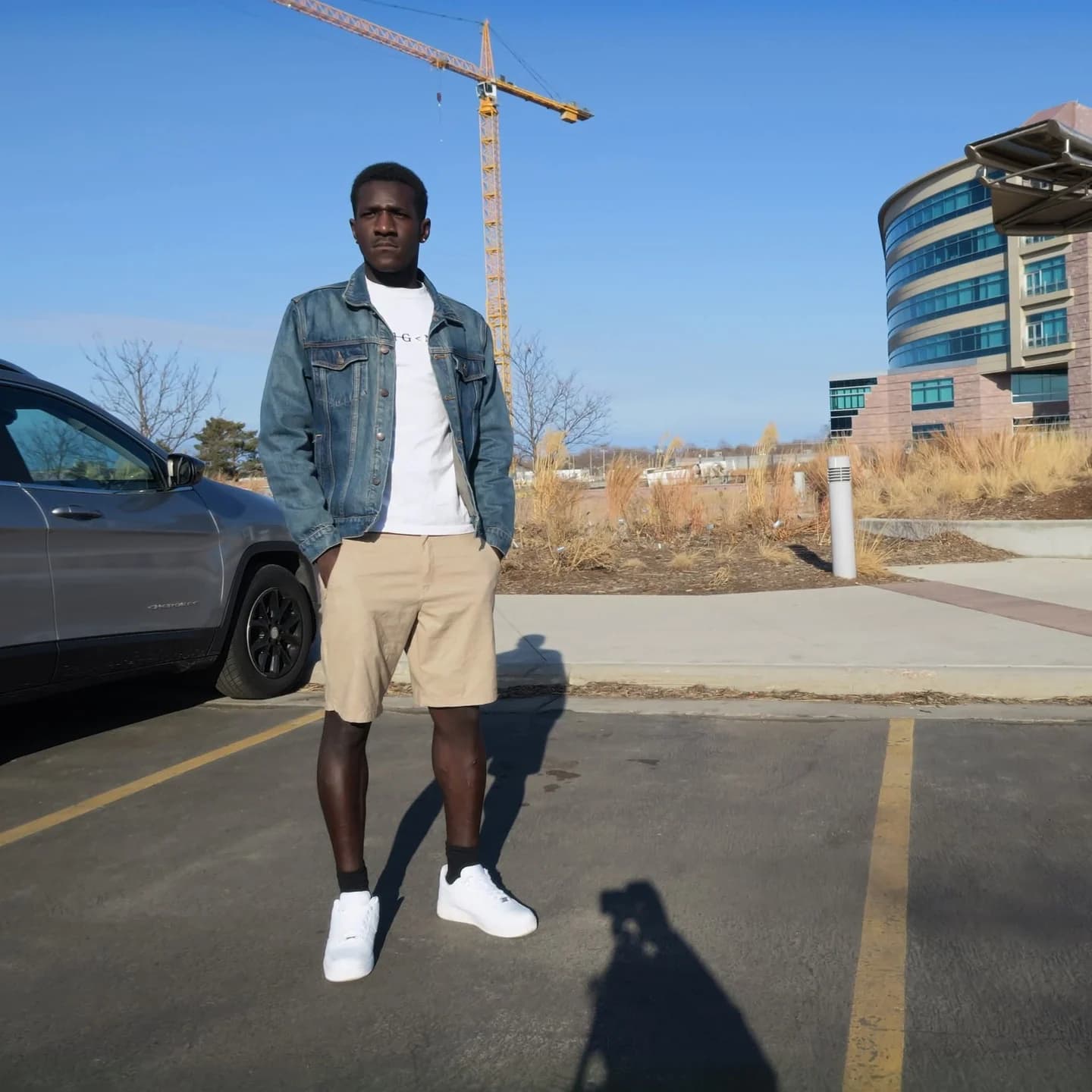 Wilson standing outdoors in a denim jacket, light shirt, tan shorts, and white shoes.